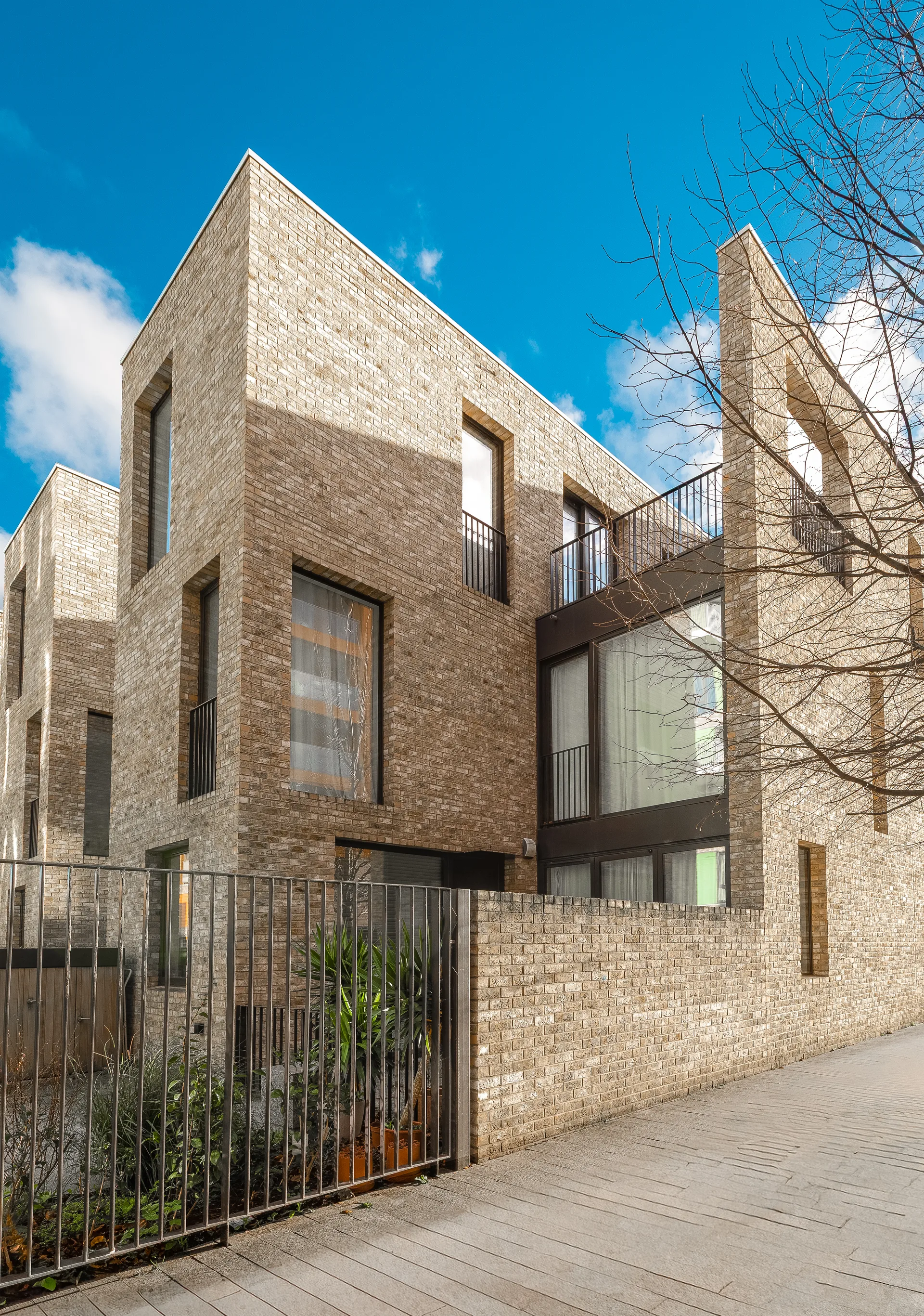 Exterior Shot Of A Modern Townhouse With Unique Angular Brick Architecture And A Dark Metal Security Fence.